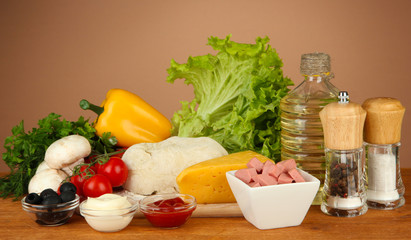 Ingredients for pizza on wooden table on brown background