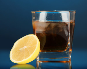 Glass of whiskey with ice and lemon on blue background