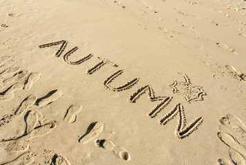 Word autumn handwritten and leaf drawn in sand