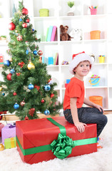 Child in Santa hat near Christmas tree with big gift