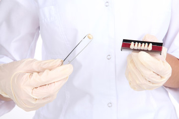 A dentists hands with denture and dental tweezers