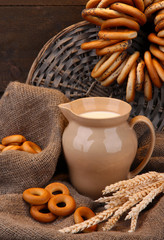jar of milk, tasty bagels and spikelets on wooden background