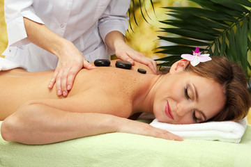 Obraz na płótnie Canvas beautiful woman in spa salon getting massage with stones,