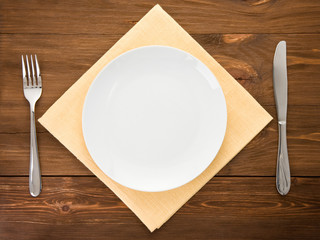 white plate, knife and fork on wood