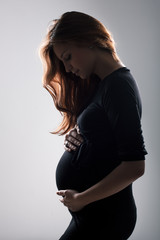 Pregnant woman holding her belly. Dramatic lighting. 