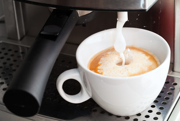 Coffee maker pouring milk foam to prepare cappuccino