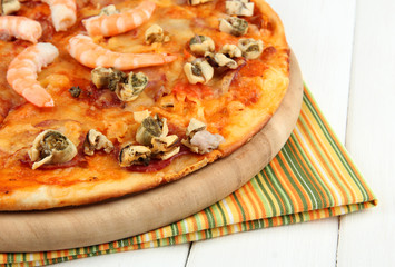 Delicious pizza with seafood on stand on wooden background