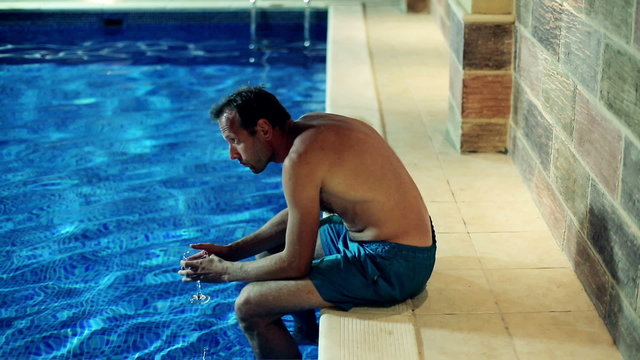 Sad man drinking wine by the swimming pool at night