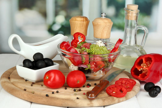 Fresh greek salad in glass bowl surrounded by ingredients for