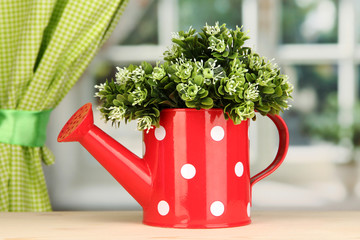 Decorative flowers in watering can on windowsill