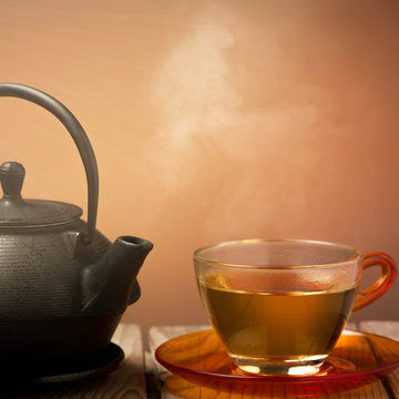 Teapot and a cup of tea on an old wooden table - hot steam smoki