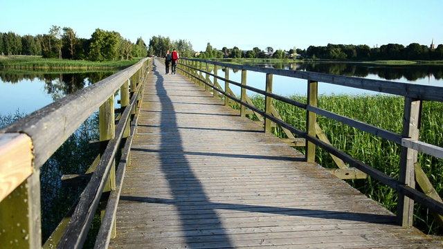 young couple walk hand in hand on wooden bridge lake