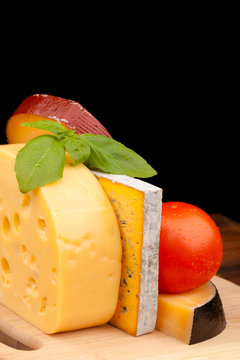 Various types of cheese on wooden table and black background