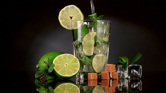 Pouring soda in mojito over dark background