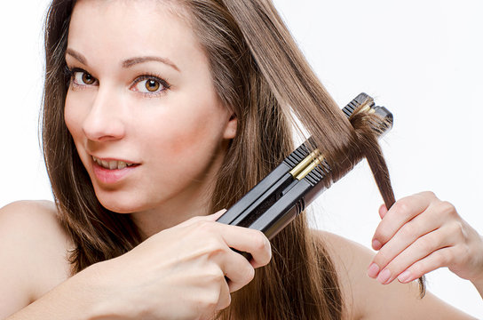 Young woman curling hair with hair straightener