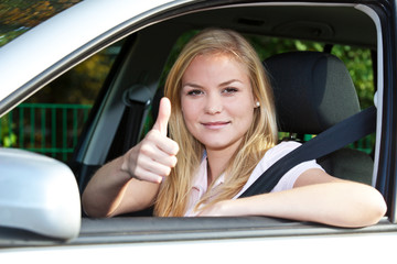 Fototapeta na wymiar Attraktive junge Frau im Auto zeigt Daumen hoch