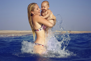 happy woman with baby boy having fun in sea water