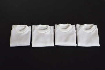 White t-shirts folded in a row on a black background.
