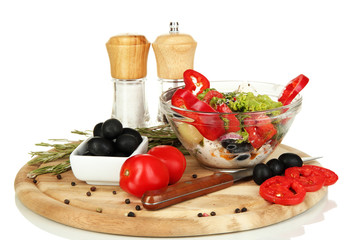 Fresh greek salad in glass bowl surrounded by ingredients for