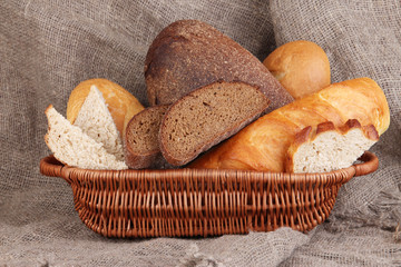 Fresh bread in basket on wooden table on sacking background