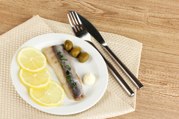 Dish of herring and lemon on plate on wooden table close-up