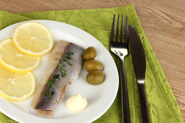 Dish of herring and lemon on plate on wooden table close-up