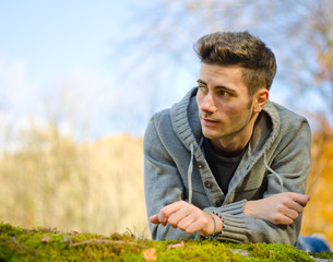 Naklejka na ściany i meble Attractive young man outdoors in nature lying on moss