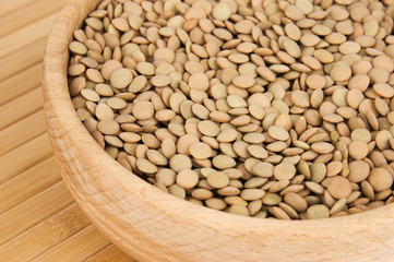 Raw lentils in wooden bowl on bamboo close-up