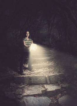 Woman Holding A Glowing Bible In The Forest