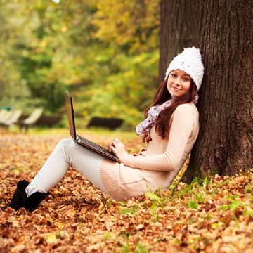 Pretty student girl with laptop in autumn park. Young European