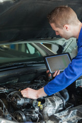 Repairman with tablet pc repairing car engine