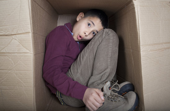 Worried teenage boy sitting in cardboard box