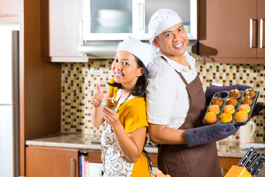 Asian Couple Baking Muffins In Home Kitchen