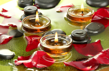 spa stones with rose petals and candles in water on plate