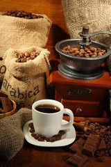 Coffee grinder and cup of coffee on brown wooden background
