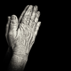 Old wrinkled hands praying isolated on black