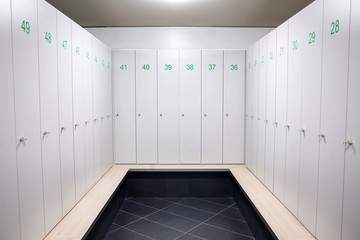 Gym dressing room with lots of white lockers with green numbers