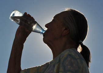 Alte Frau trinkt Mineralwasser an einem heißen Tag