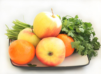 Apples, tangerines and greens lie on a dish