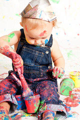 süßes kleines Kind in Latzhosen mit Pinseln und Farben