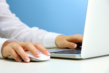 female hands writing on laptot, on blue background