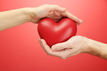 Obraz premium Red heart in woman and man hands, on red background