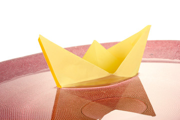 Color paper ship in water on pink plate, close-up