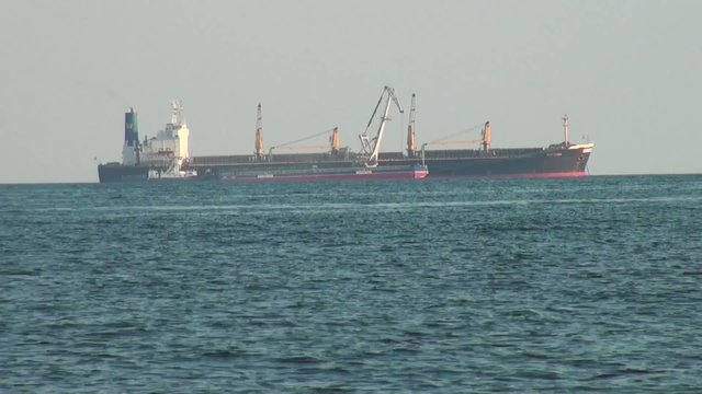 Cargo ship and small ship floating at surface of sea