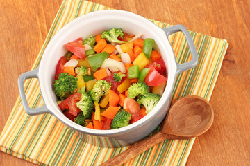 Vegetable stew in gray pot on color napkin on wooden background