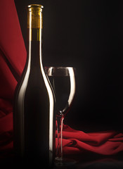 Red wine glass and bottle on a silk background