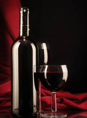 Red wine glass and bottle on a silk background