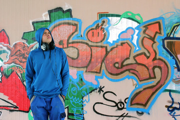 Jugendkultur : Jugendlicher  mit Kapuzenshirt und Kopfhörer steht vor seiner gesprühten Graffitiwand