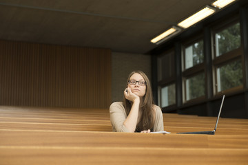 Eine junge Studentin sitzt alleine mit Notebook im Hörsaal