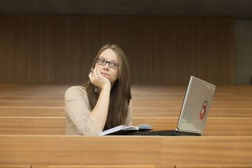 Eine junge Studentin sitzt alleine mit Notebook im Hörsaal